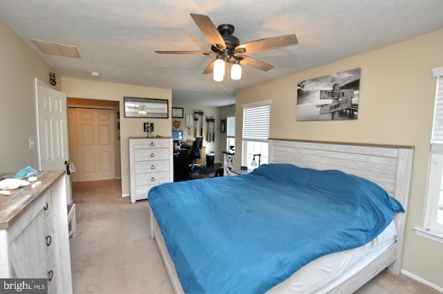 bedroom with a textured ceiling, light colored carpet, a closet, and ceiling fan