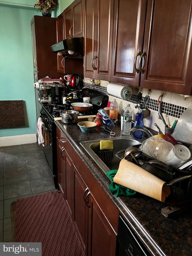 kitchen with tasteful backsplash, sink, black range oven, and dark tile patterned flooring