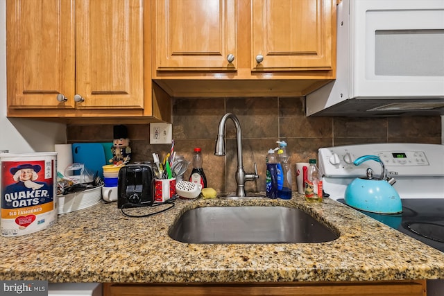 kitchen featuring stone countertops, white appliances, backsplash, and sink