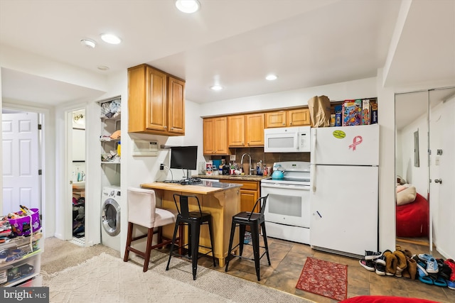 kitchen with a breakfast bar, white appliances, backsplash, sink, and washer / dryer