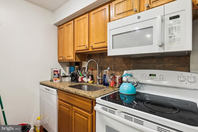 kitchen featuring white appliances, light stone counters, and sink