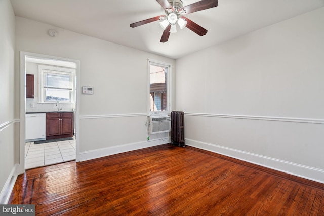 empty room with hardwood / wood-style flooring, cooling unit, sink, radiator heating unit, and ceiling fan