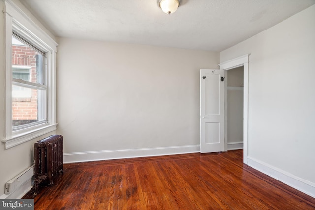 spare room featuring dark hardwood / wood-style flooring, a baseboard heating unit, a textured ceiling, and radiator