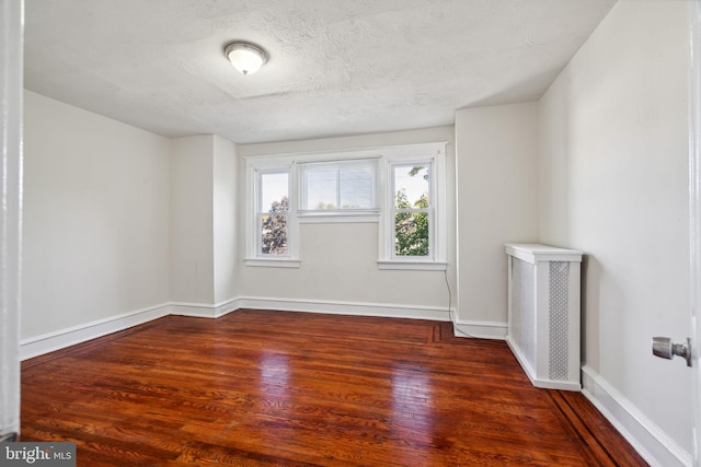 unfurnished room with a textured ceiling, radiator heating unit, and dark hardwood / wood-style floors