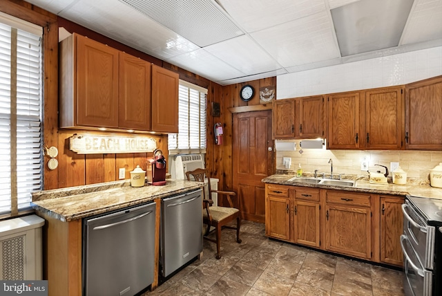 kitchen with wood walls, sink, appliances with stainless steel finishes, light stone counters, and tasteful backsplash