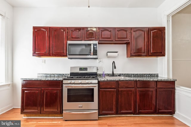 kitchen featuring light hardwood / wood-style floors, dark stone countertops, stainless steel appliances, and sink