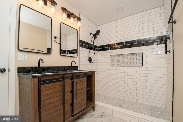 bathroom with marble finish floor, a tile shower, and a sink