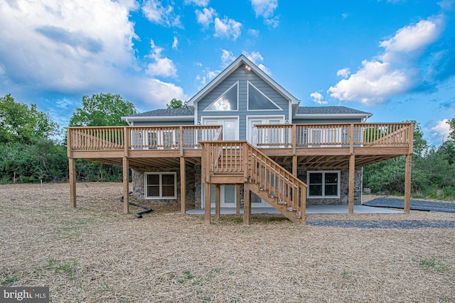 rear view of property with stone siding, a patio area, stairway, and a deck