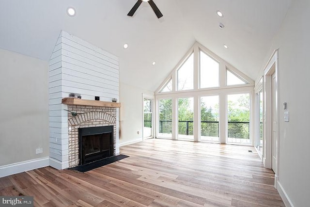 unfurnished living room with high vaulted ceiling, a ceiling fan, wood finished floors, baseboards, and a brick fireplace