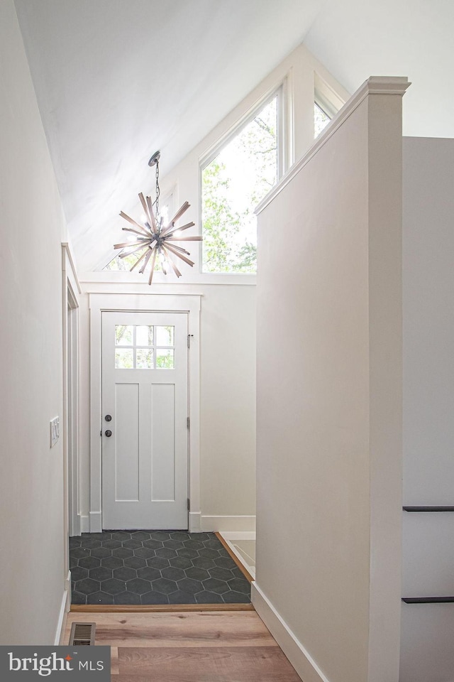 doorway with lofted ceiling, wood finished floors, a wealth of natural light, and a notable chandelier