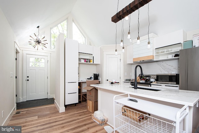 kitchen with high vaulted ceiling, open shelves, a chandelier, light wood finished floors, and stainless steel microwave