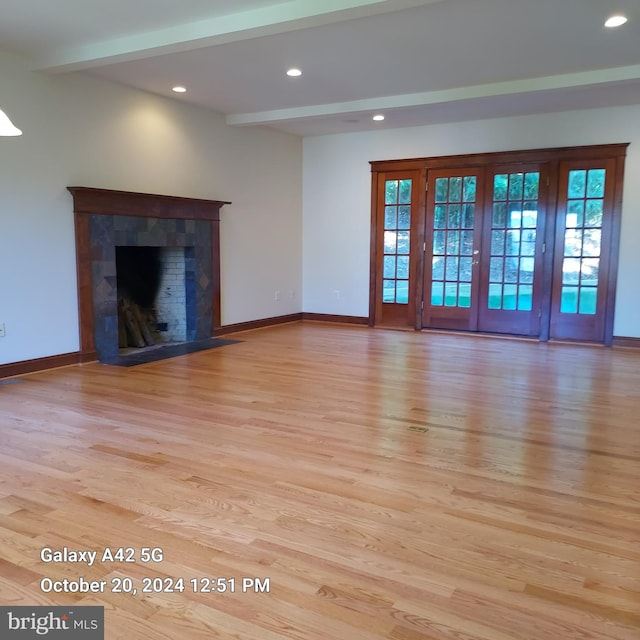 unfurnished living room featuring a healthy amount of sunlight, a tile fireplace, beam ceiling, and light hardwood / wood-style floors