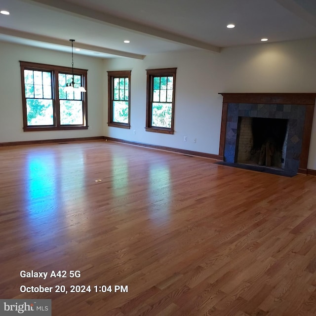 unfurnished living room with hardwood / wood-style flooring, beamed ceiling, and a tile fireplace