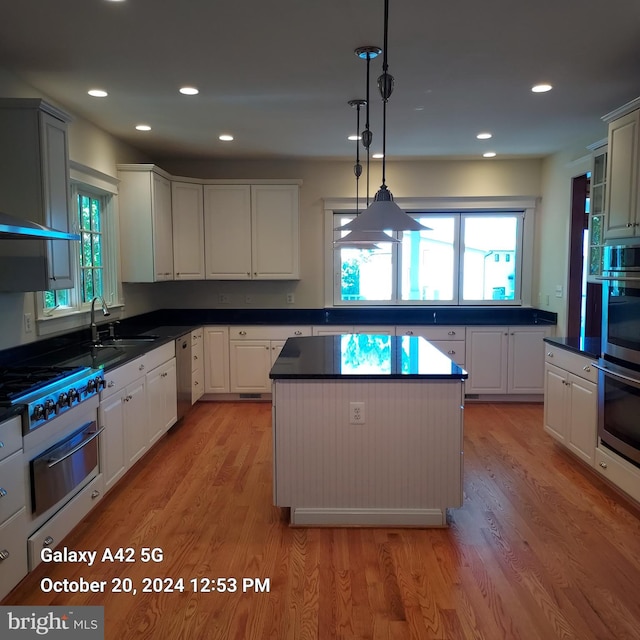 kitchen with white cabinetry, light wood-type flooring, a center island, sink, and decorative light fixtures