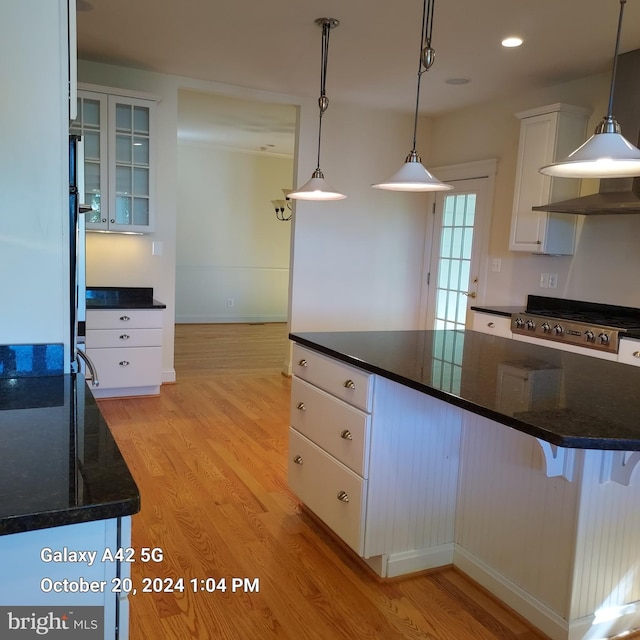 kitchen with light wood-type flooring, a kitchen island, dark stone counters, pendant lighting, and white cabinets