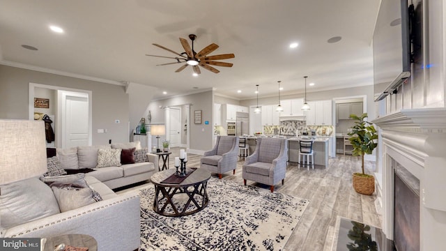 living room featuring a fireplace, light hardwood / wood-style flooring, ceiling fan, and ornamental molding