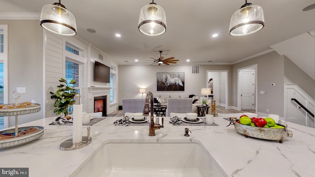 kitchen with ceiling fan, sink, light stone counters, decorative light fixtures, and ornamental molding