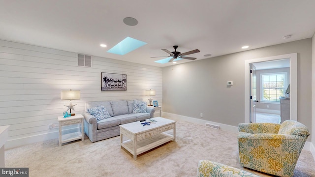 carpeted living room featuring a skylight, ceiling fan, and wood walls