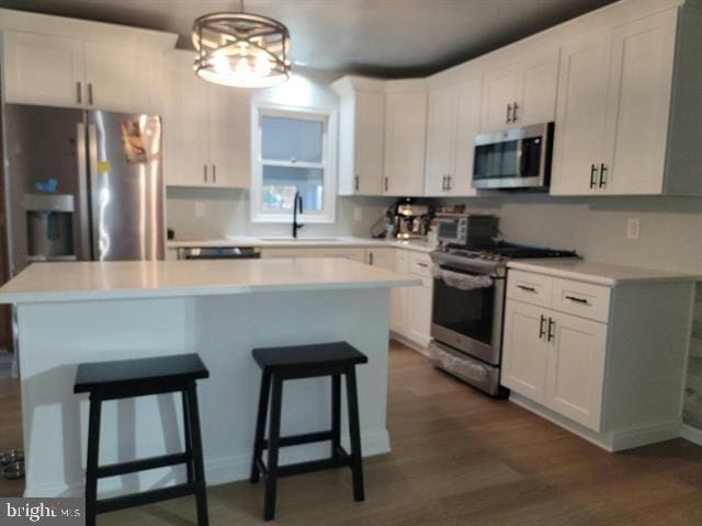 kitchen with hanging light fixtures, appliances with stainless steel finishes, white cabinetry, dark hardwood / wood-style floors, and sink