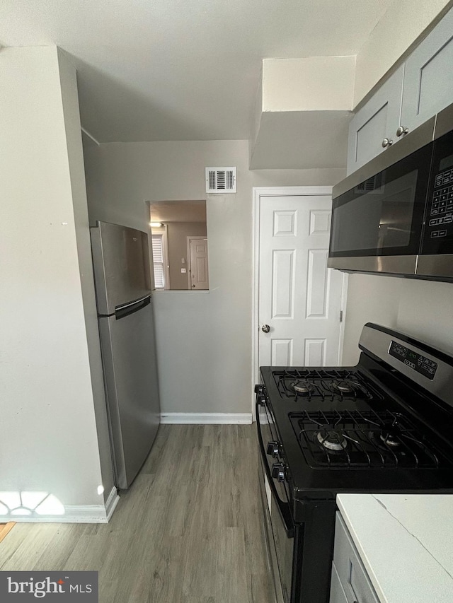 kitchen with appliances with stainless steel finishes, light hardwood / wood-style floors, and gray cabinetry