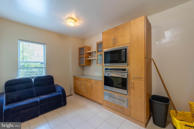 kitchen with light stone countertops, oven, light tile patterned floors, and black microwave