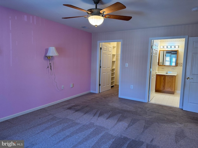 unfurnished bedroom with light carpet, a walk in closet, ensuite bath, and ceiling fan