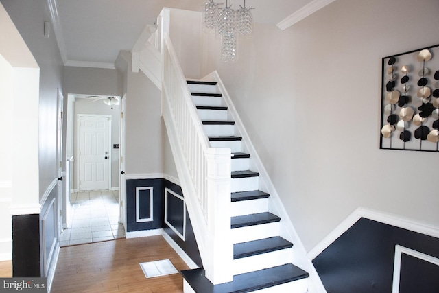 stairs with an inviting chandelier, ornamental molding, and wood-type flooring