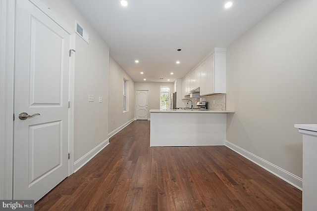 kitchen with kitchen peninsula, white cabinets, backsplash, dark wood-type flooring, and sink