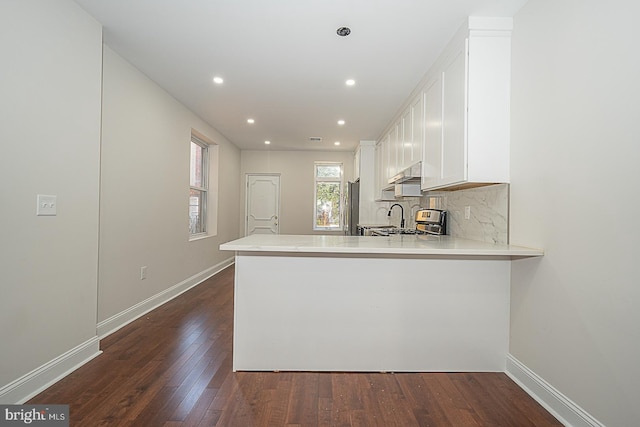 kitchen featuring kitchen peninsula, white cabinetry, stainless steel appliances, decorative backsplash, and dark hardwood / wood-style floors