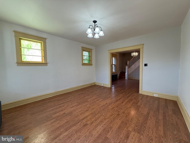 spare room featuring dark wood-type flooring, a notable chandelier, and a healthy amount of sunlight