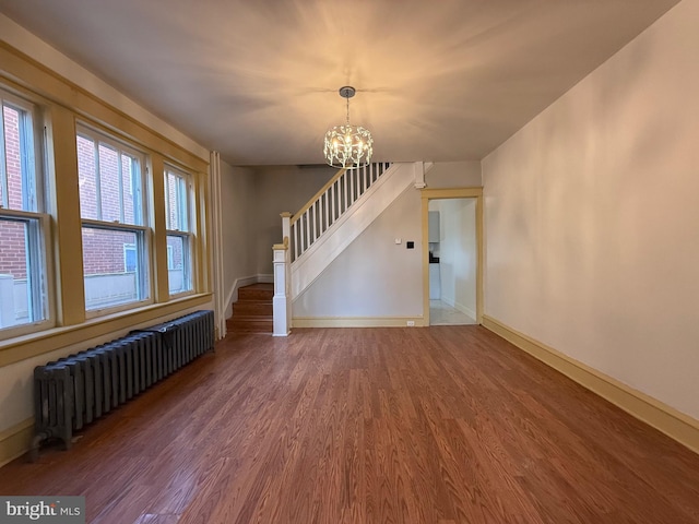 unfurnished living room with a chandelier, wood-type flooring, and radiator