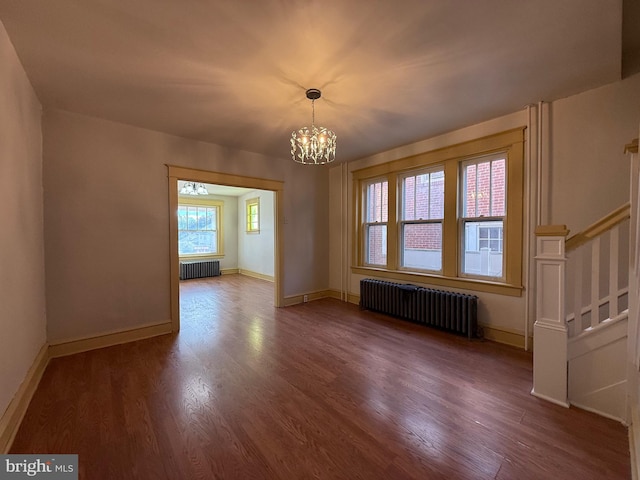 empty room featuring dark wood-type flooring, radiator heating unit, and a chandelier