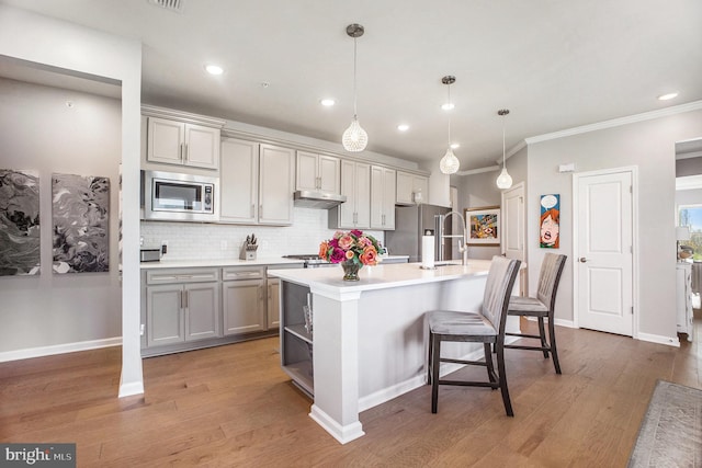 kitchen featuring dark hardwood / wood-style floors, stainless steel appliances, a center island with sink, crown molding, and decorative light fixtures