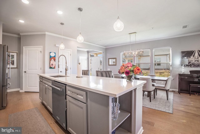 kitchen with an island with sink, appliances with stainless steel finishes, light hardwood / wood-style flooring, sink, and decorative light fixtures