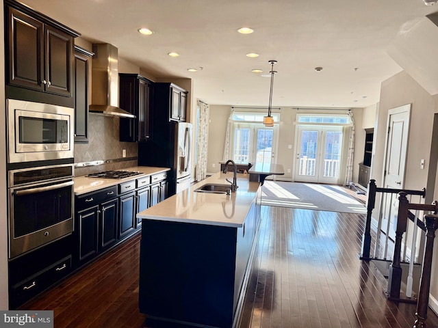 kitchen with sink, wall chimney exhaust hood, french doors, a kitchen island with sink, and appliances with stainless steel finishes