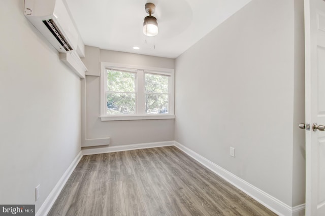 spare room with an AC wall unit, light hardwood / wood-style flooring, and ceiling fan