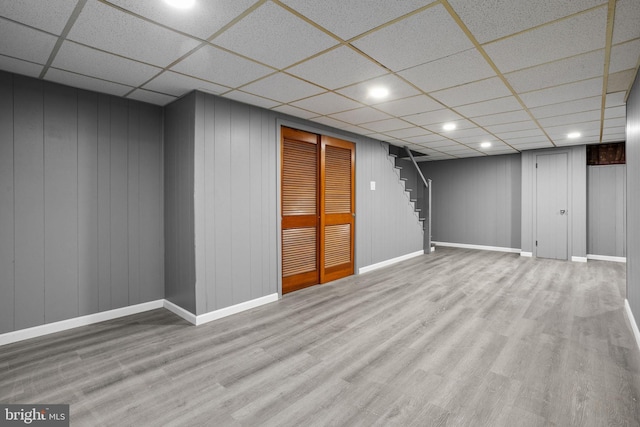 basement with a paneled ceiling, light hardwood / wood-style floors, and wood walls