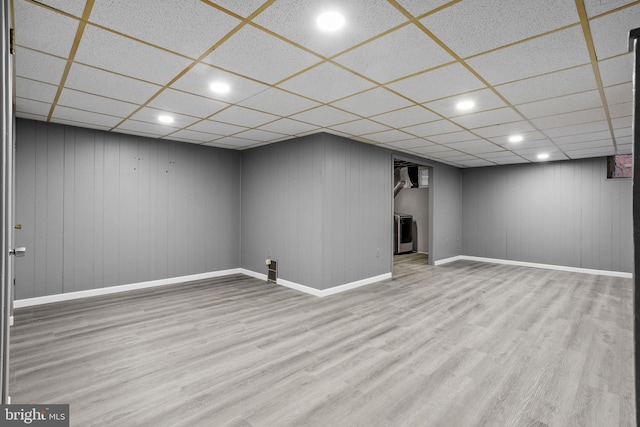 basement with light hardwood / wood-style flooring, wood walls, and a paneled ceiling