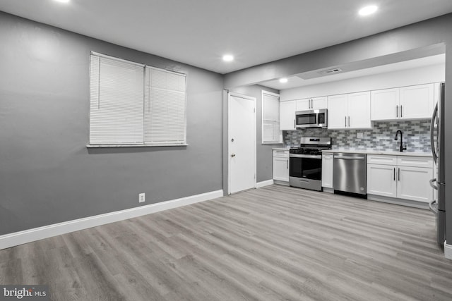 kitchen featuring decorative backsplash, white cabinetry, light wood-type flooring, sink, and stainless steel appliances