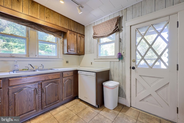 kitchen with sink, dishwasher, light tile patterned floors, and wood walls