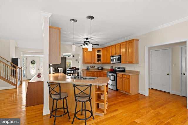 kitchen with kitchen peninsula, appliances with stainless steel finishes, light wood-type flooring, a kitchen breakfast bar, and sink