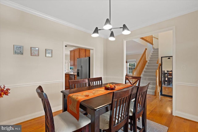 dining space with light hardwood / wood-style flooring, ornamental molding, and an inviting chandelier