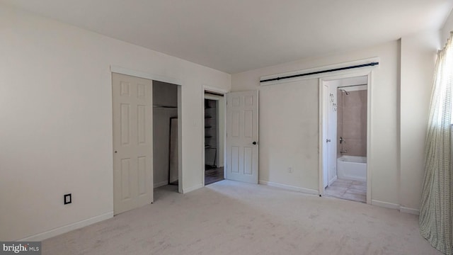 unfurnished bedroom with light carpet, a closet, and ensuite bath