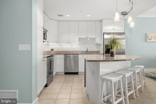 kitchen with decorative backsplash, a kitchen island, stainless steel appliances, stone counters, and white cabinets