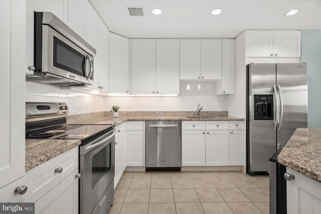 kitchen with light stone countertops, appliances with stainless steel finishes, white cabinets, decorative backsplash, and light tile patterned floors