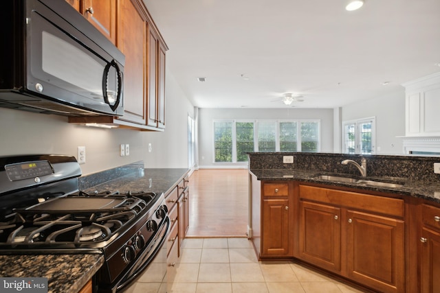 kitchen featuring black appliances, sink, ceiling fan, dark stone counters, and light tile patterned floors