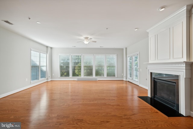 unfurnished living room featuring baseboard heating, a healthy amount of sunlight, light wood-type flooring, and ceiling fan