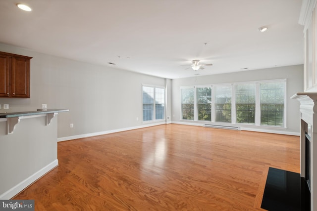 unfurnished living room with ceiling fan, baseboard heating, and light wood-type flooring