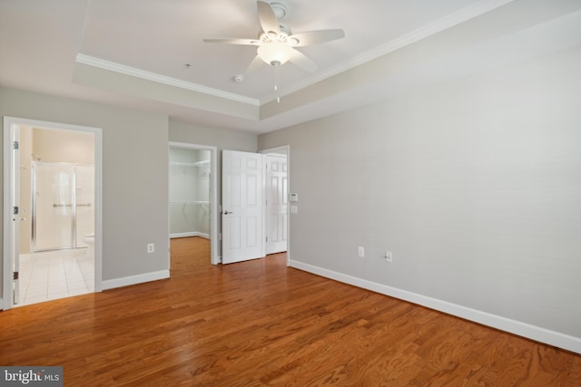 unfurnished bedroom with ensuite bathroom, a raised ceiling, light hardwood / wood-style floors, ceiling fan, and crown molding