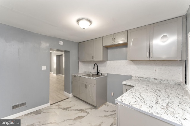 kitchen featuring gray cabinets, decorative backsplash, sink, and light stone counters